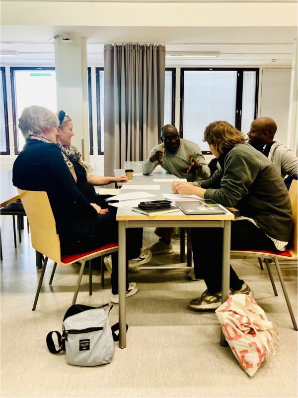 An image depicting five people sitting around a table talking to each other.