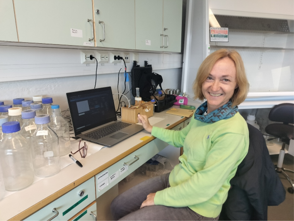 En kvinna sitter vid en dator i ett laboratorium. Hon tittar mot kameran och ler.