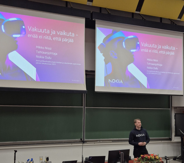 En man talar framför projektorskärmar.