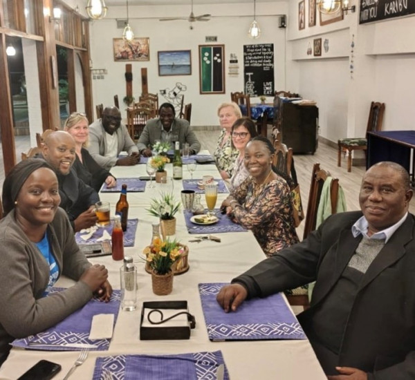 Personer runt ett bord på en restaurang. Alla ser in i kameran och ler.