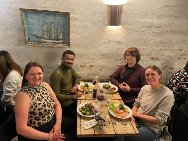 A group of people having dinner at a table. Everyone is looking into the camera and smiling.