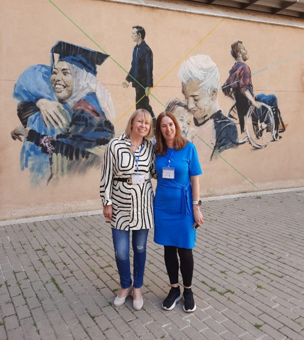 Two women standing next to each other in front of a mural.