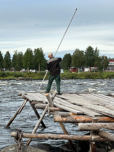 En man håvfiskar på en träbrygga i en fors.