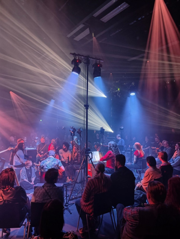 En bild från en konsert där musikern är i mitten och publiken omger dem i en cirkel. Orangea och blå spotlights lyser upp artisten.