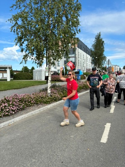 En kvinna iklädd röd t-shirt och jeansshorts står på en gata och viftar med en röd flagga.